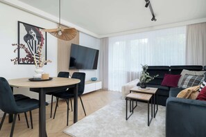 Ein modernes Wohnzimmer mit Essbereich, einem an der Wand montierten Flachbildfernseher und einer Couch mit Kissen.