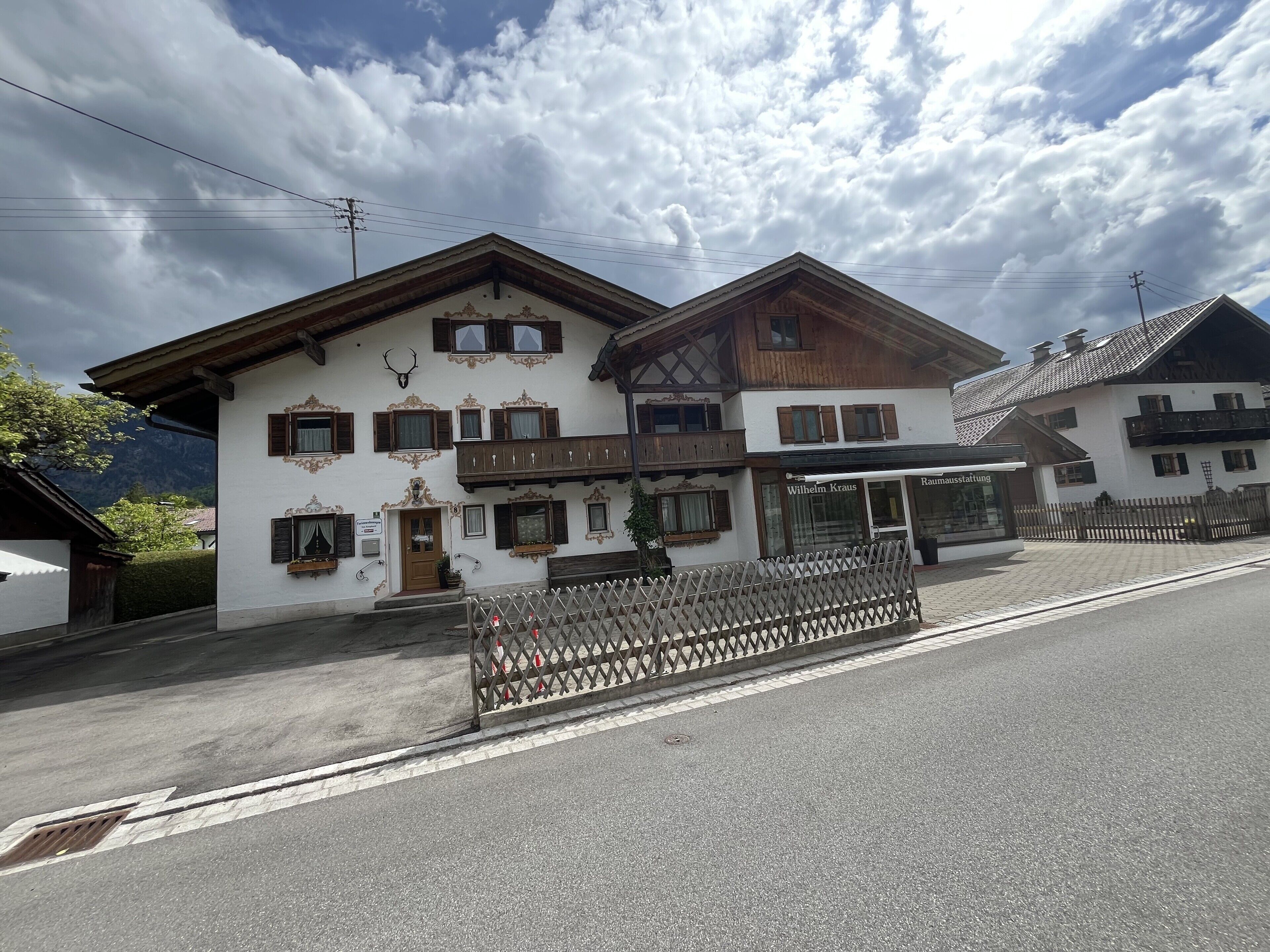 Un bâtiment de style chalet traditionnel, doté d’un balcon en bois, d’une enseigne indiquant « Wilhelm Kraus » et d’une clôture en bois à l’avant.