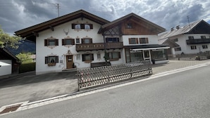 Un edificio de estilo chalete tradicional con balcón de madera, un cartel con el nombre 'Wilhelm Kraus' y una cerca de madera al frente.