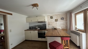 Una cocina compacta con una isla de madera, armarios blancos, horno empotrado y ventana con persianas.