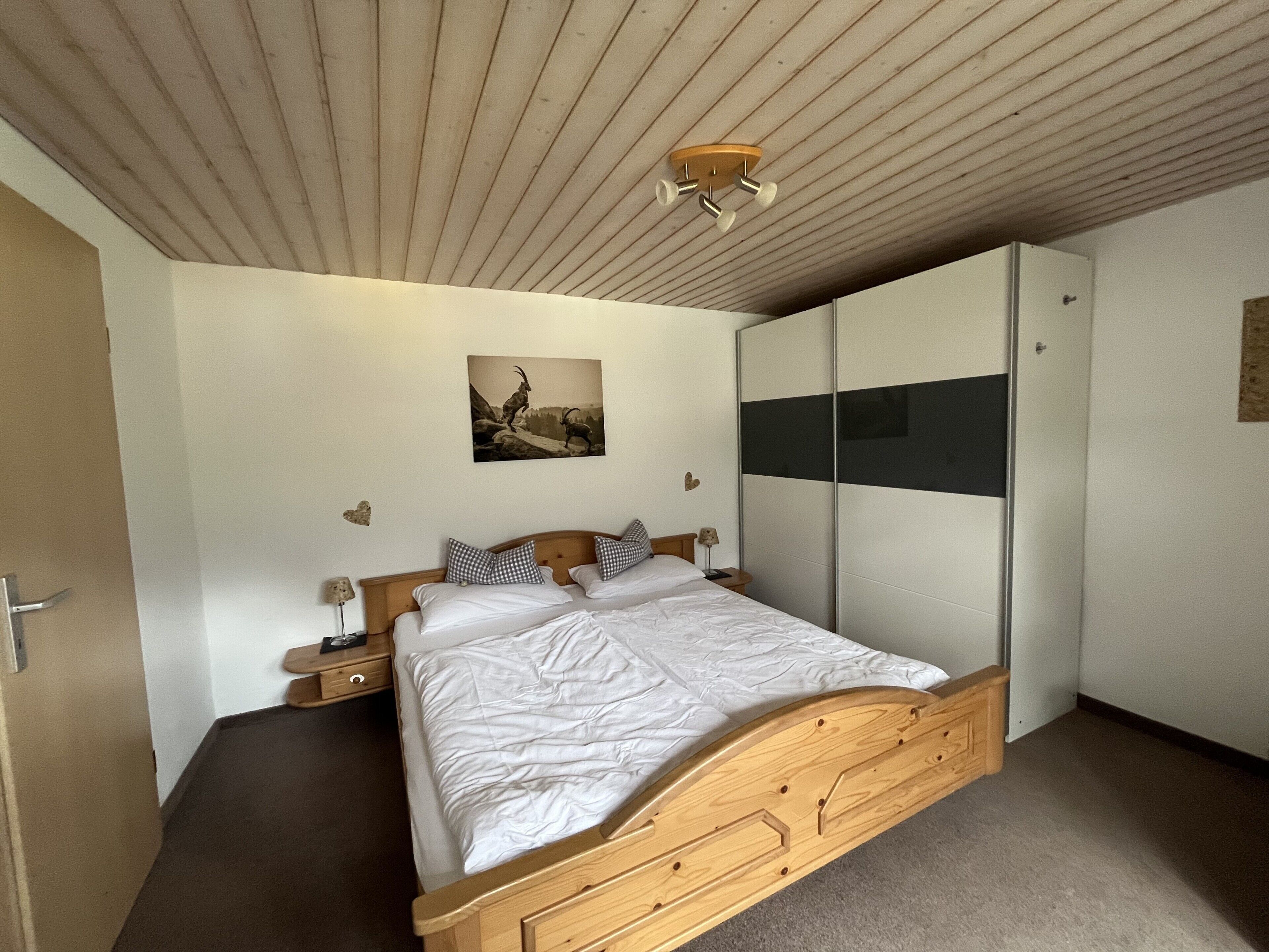 Ein Schlafzimmer mit einem hölzernen Bett, einem Nachttisch, einem Kleiderschrank und einem Deckenventilator.