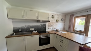 Una cocina con armarios blancos, encimera de madera, estufa y ventana con vistas a zonas verdes.