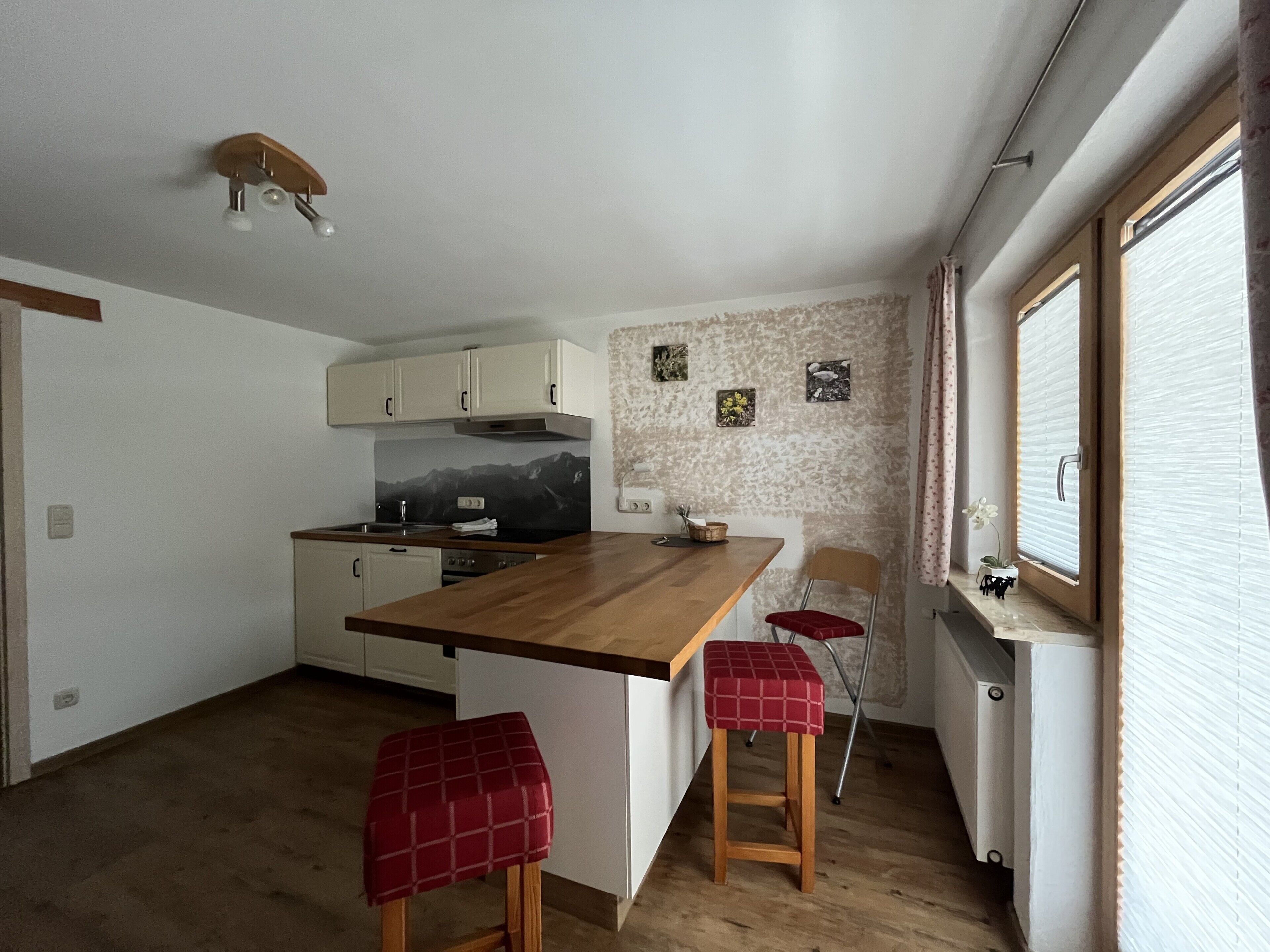 A compact kitchen with a wooden island, two stools, a stove, and a refrigerator.