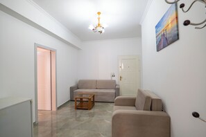 A living room with a beige sofa, a wooden coffee table, a chandelier, and a door with a painting. - Grace Corner (Sarande)