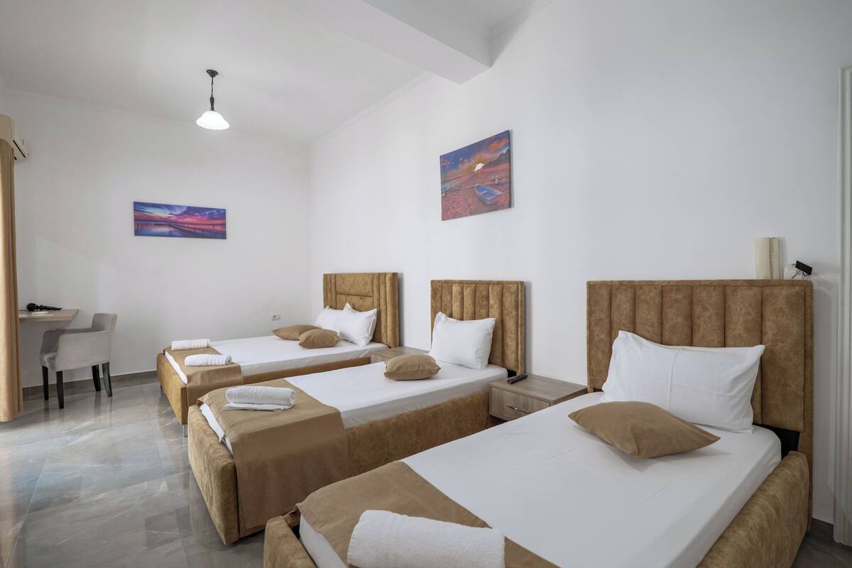 Una habitación de hotel con tres camas individuales, un escritorio y una silla.