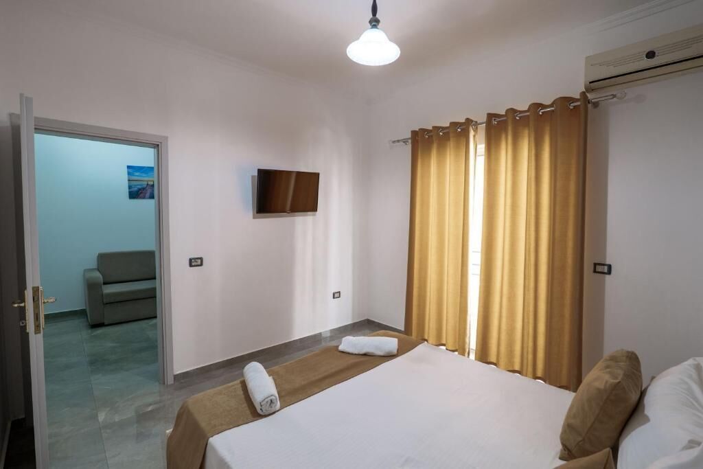 Een hotelkamer met een bed, een televisie, een raam met gordijnen en een deur naar een gang.
