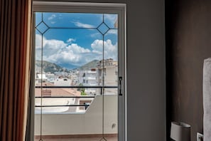 A room with a view through a window with a geometric design, a door, and a wall-mounted lamp. - Grace Corner (Sarande)