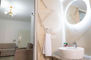 Un bagno con parete in marmo, uno specchio rotondo, un lavabo e un portasciugamani.