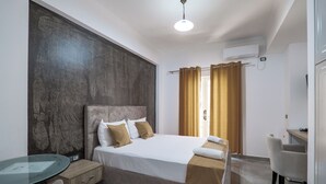 A hotel room with a bed, a glass table, a chair, a desk, and a window with curtains. - Grace Corner  (Sarande)