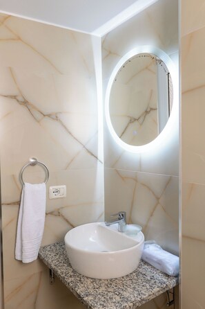 A bathroom with a marble wall, a sink with a mirror, and a towel rack.
