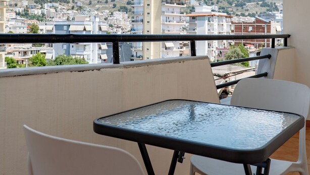 A balcony with a table and chairs, overlooking a cityscape with buildings and hills. - Grace Corner  (Sarande)