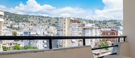 Un balcone con tavolo e sedie, affacciato su una città con edifici e colline.