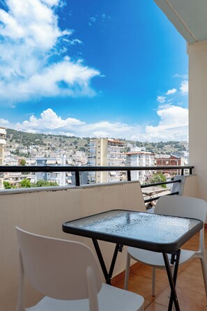 Un balcone con tavolo e sedie, affacciato su una città con edifici e colline.