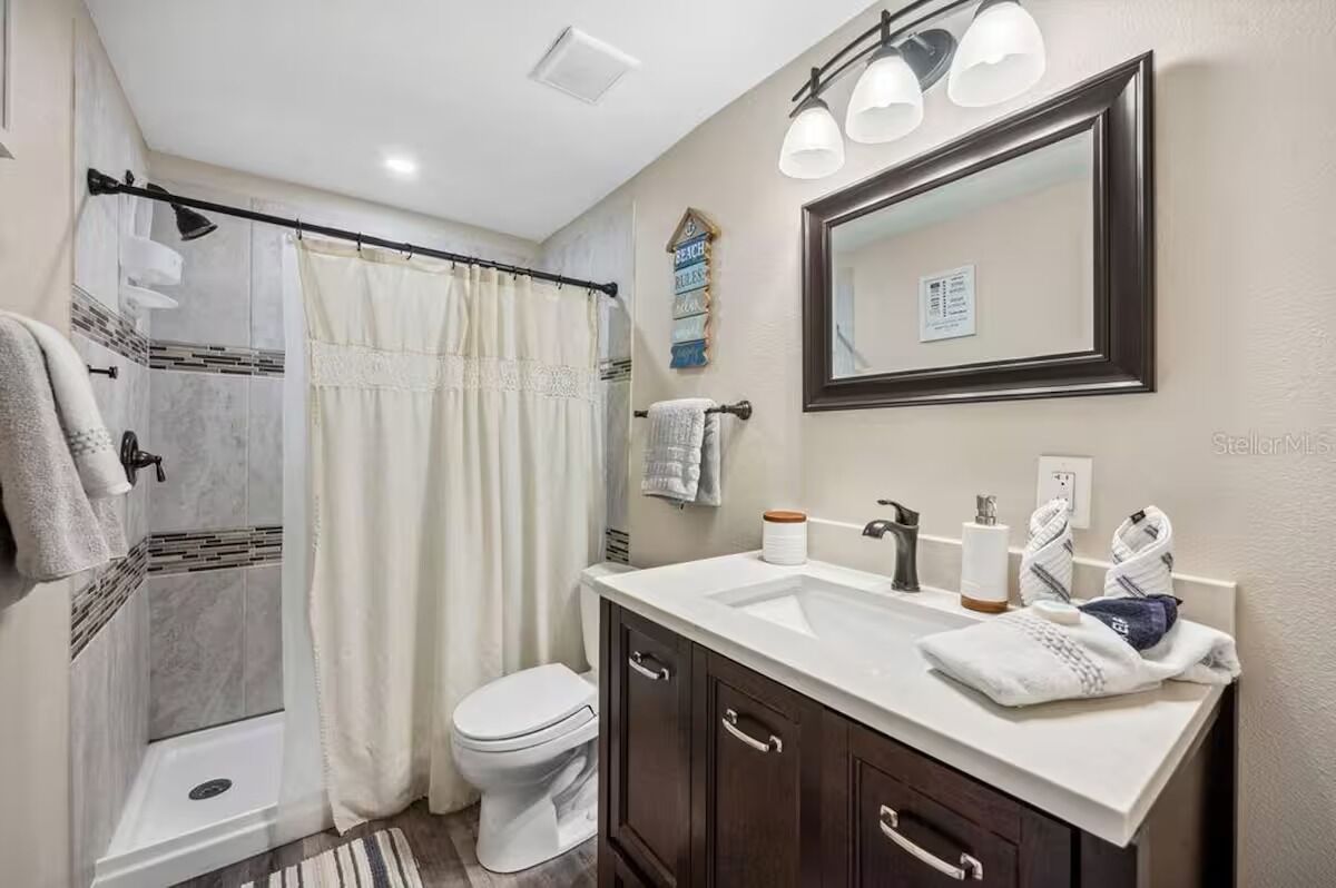 A bathroom with a shower, toilet, vanity, and a mirror.