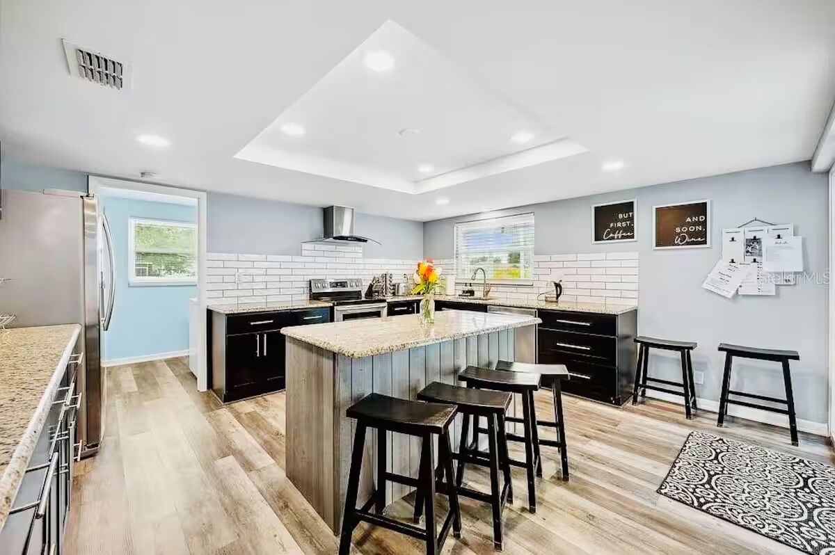 A modern kitchen with a central island, black bar stools, and a window with a view.