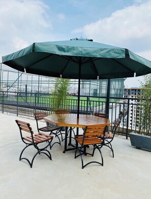 A round wooden table with six chairs and a large green umbrella. - Spacious Fully-stocked modern studio with a gym, cafe, & pitch in Kileleshwa (Nairobi)
