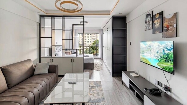 A modern living room with a sofa, coffee table, TV, and a view of a balcony. - Spacious Fully-stocked modern studio with a gym, cafe, & pitch in Kileleshwa (Nairobi)