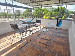 Un patio techado al aire libre con una mesa, sillas, una hamaca y vistas a la vegetación.