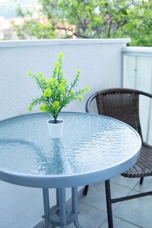Een ronde glazen tafel met een potplant, een rieten stoel en een witte muur op de achtergrond.
