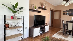 Ein modernes Wohnzimmer mit Fernseher, Holzmöbeln und Zimmerpflanzen.