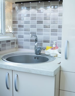 Een keuken met een spoelbak, een raam en een betegelde achterwand.