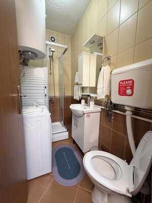Une salle de bain équipée d’une douche, de toilettes, d’un lavabo et d’un panneau indiquant qu’il est interdit de jeter des objets non biodégradables dans les toilettes.
