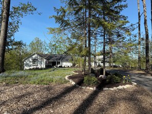 Et etplanshus med en veranda, omgivet af skov og en velplejet have.