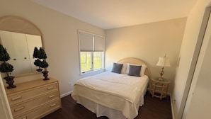 Un dormitorio con cama, cómoda, espejo, ventana y mesita de noche.
