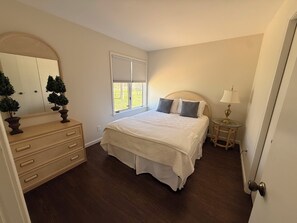 Un dormitorio con cama, cómoda, espejo, ventana y mesita de noche.