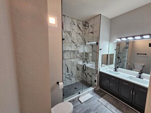 Un baño moderno con ducha de vidrio, un espejo grande y un lavamanos con gabinete.