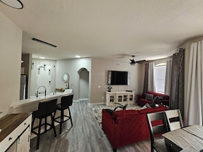 Ein modernes Wohnzimmer mit einem roten Sofa, einem Fernseher und einem Essbereich mit einer Bar.