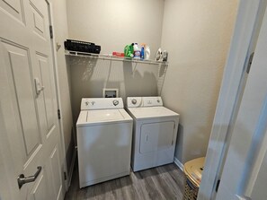 A laundry room with two stacked washers and dryers, a shelf with cleaning supplies, and a basket. - Newly Renovated!  4-bedroom with pool near Disney and Universal Parks (Davenport)