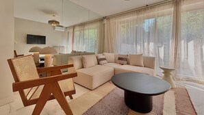 Ein modernes Wohnzimmer mit einem Ecksofa, einem runden Couchtisch, einem Holzstuhl und einem an der Wand befestigten Fernseher.