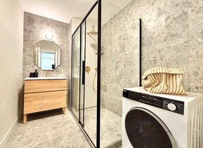 Une salle de bain moderne avec un meuble-lavabo en bois, une cabine de douche en verre et un lave-linge.