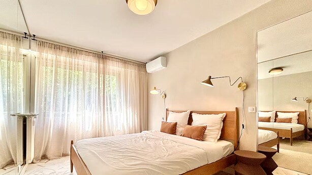 Ein modernes Schlafzimmer mit einem großen Bett, einem Spiegel und einem Fenster mit durchsichtigen Vorhängen.