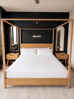 Une chambre moderne avec un lit à baldaquin en bois, deux tables de chevet, un grand miroir et un panneau lumineux au néon sur le mur.
