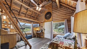 Interno di una baita di legno con un letto, una scrivania e vista sulla natura.