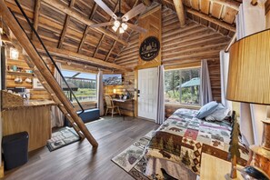 Ein Interieur einer Blockhütte mit Bett, Schreibtisch und Blick ins Freie.