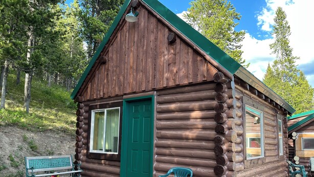 Una baita di legno con una porta verde, una panchina e un portico con sedie di plastica.