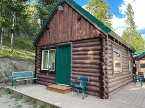 Eine Blockhütte mit grüner Tür, einer Bank und einer Veranda mit Plastikstühlen.
