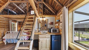 Interno di una baita con letto a soppalco, angolo cottura e un'ampia finestra.