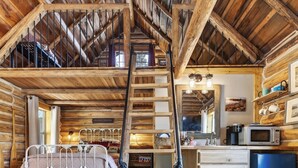 Ambiente rustico con camera da letto in soppalco, una scala in legno, una cucina con frigorifero blu e un'area pranzo.