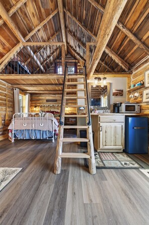 Ein rustikales Interieur mit Schlafzimmer im oberen Bereich, einer Holzleiter, einer Küche mit blauem Kühlschrank und einem Essbereich.