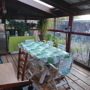 Un patio techado con una mesa y sillas, plantas en macetas y vistas del entorno.