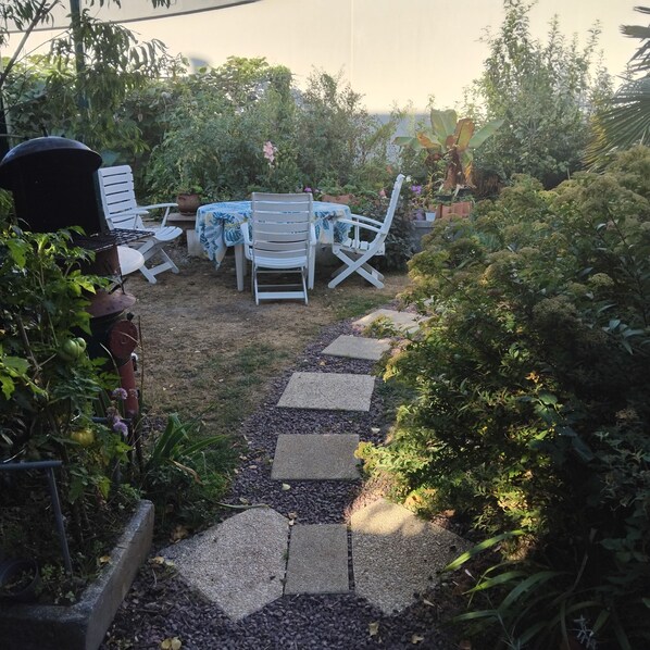 Un patio jardín con mesa y sillas, rodeado de plantas y un camino de grava.