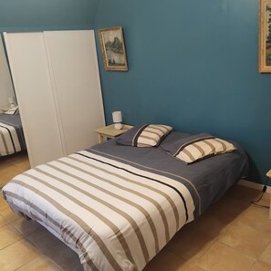 Un dormitorio con cama, mesita de noche, lámpara y un cuadro en la pared.