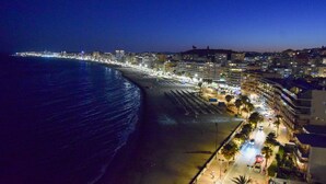 Eine Küstenstadt bei Nacht mit Strand, beleuchteten Gebäuden und freiem Blick auf den Ozean.