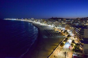 Eine Küstenstadt bei Nacht mit Strand, beleuchteten Gebäuden und freiem Blick auf den Ozean.