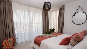 Ein Schlafzimmer mit einem Bett, Vorhängen, einer Pendelleuchte und einem runden Spiegel an der Wand.