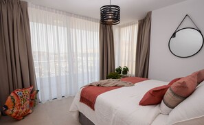 Ein Schlafzimmer mit einem Bett, Vorhängen, einer Pendelleuchte und einem runden Spiegel an der Wand.